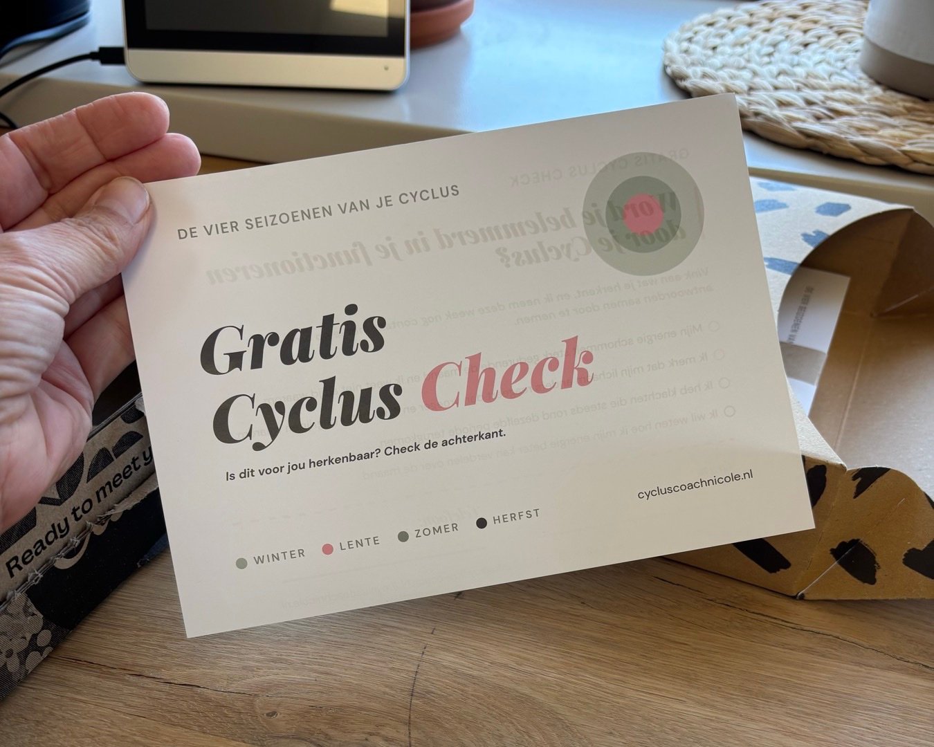 Hand houdt de kaart “Gratis Cyclus Check” vast, met de vier seizoenen winter, lente, zomer en herfst