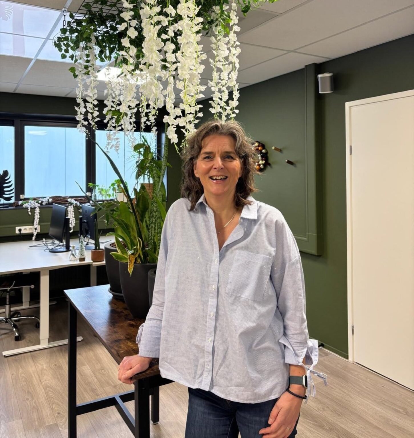 Nicole staat lachend in een lichte werkruimte met planten